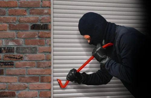 Vermummter Einbrecher mit Brechstange an Rolladen