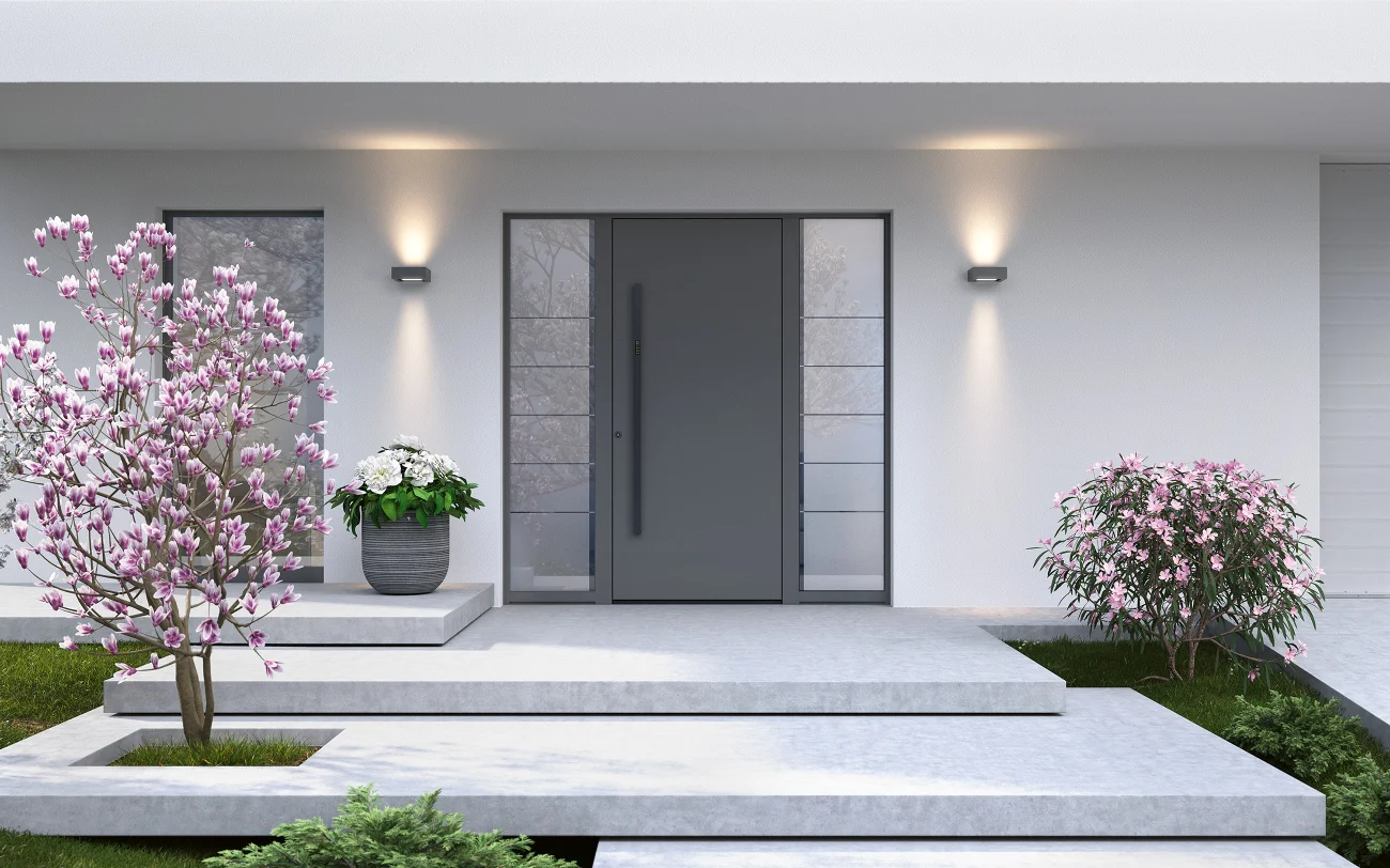 Moderne und hochwertige Aluminium Haustür mit Glaspaneelen an den Seiten in moderner Hausfassade mit blühendem Vorgarten